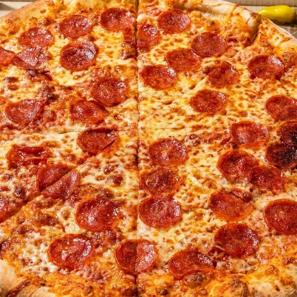 A large pepperoni pizza, sliced, in a cardboard box with yellow peppers.