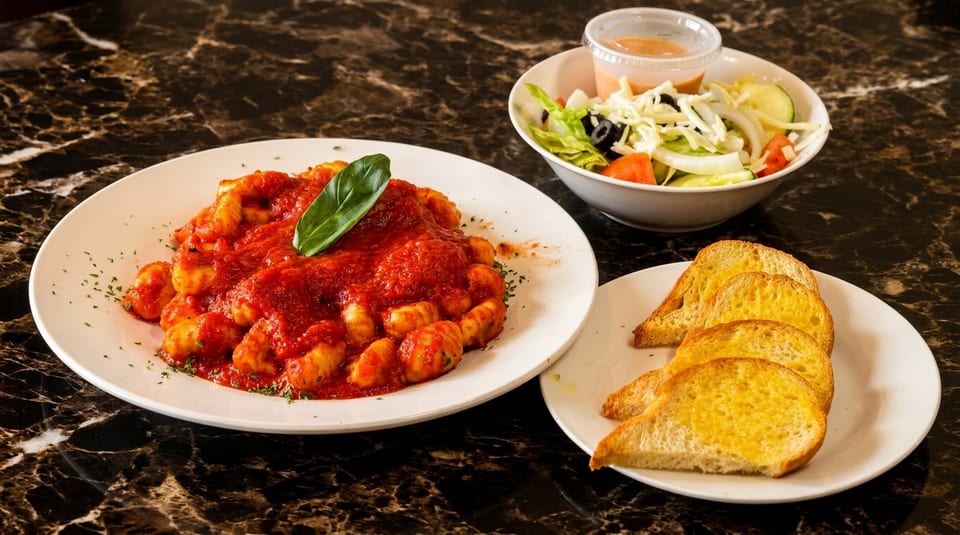 Gnocchi with red sauce and basil, a side salad, and garlic bread on a marble table.