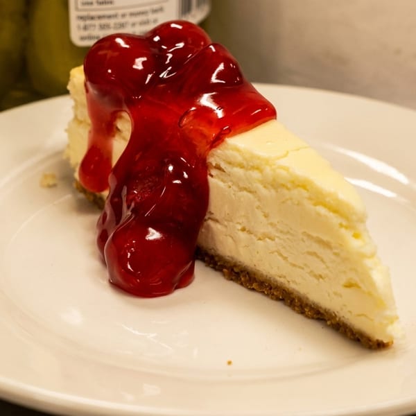Slice of cheesecake with cherry topping on a white plate, with a blurred background.