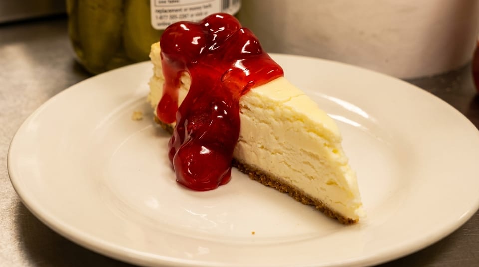 Slice of cheesecake with cherry topping on a white plate, with a blurred background.
